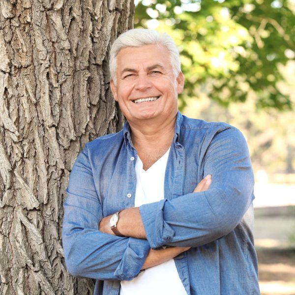 Older man leans against tree near pleasant grove