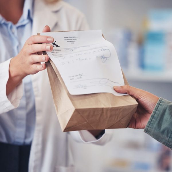 Pharmacist hands prescription refill bag to customer
