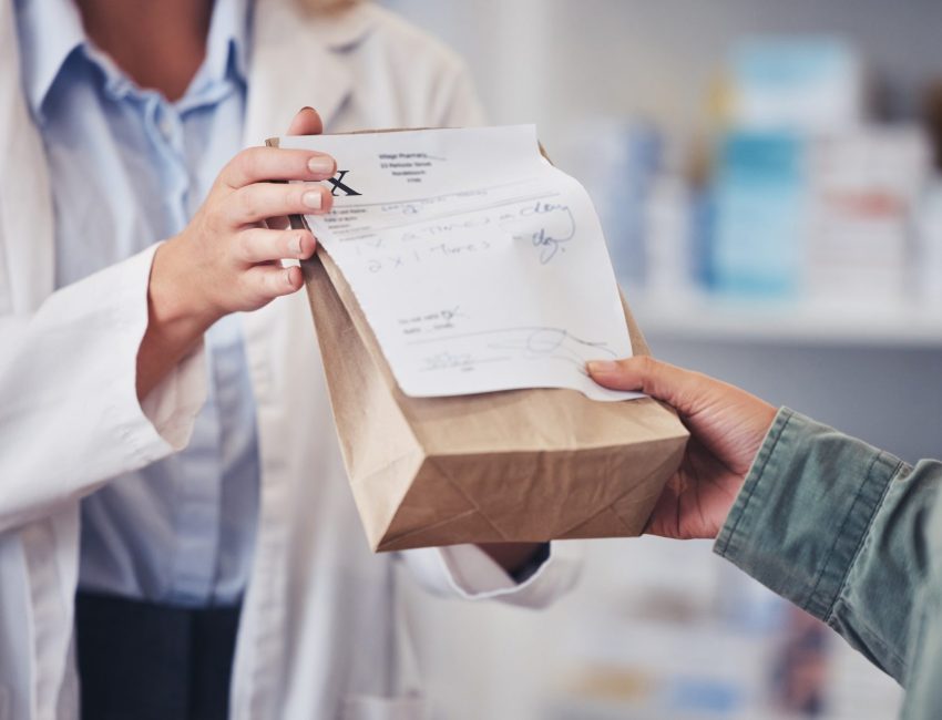 Pharmacist hands prescription refill bag to customer